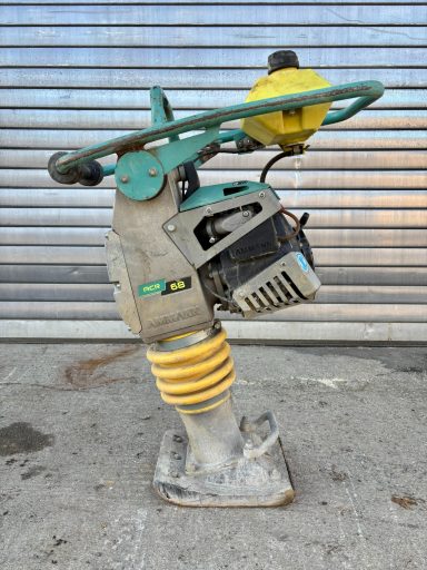 Bodenverdichter mit gelbem Schwingkörper und grünem Handgriff, auf Betonuntergrund.